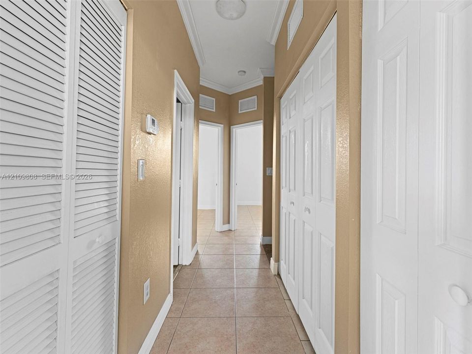 Hallway featuring tile flooring, crown molding, and multiple sets of bi-fold closet doors
