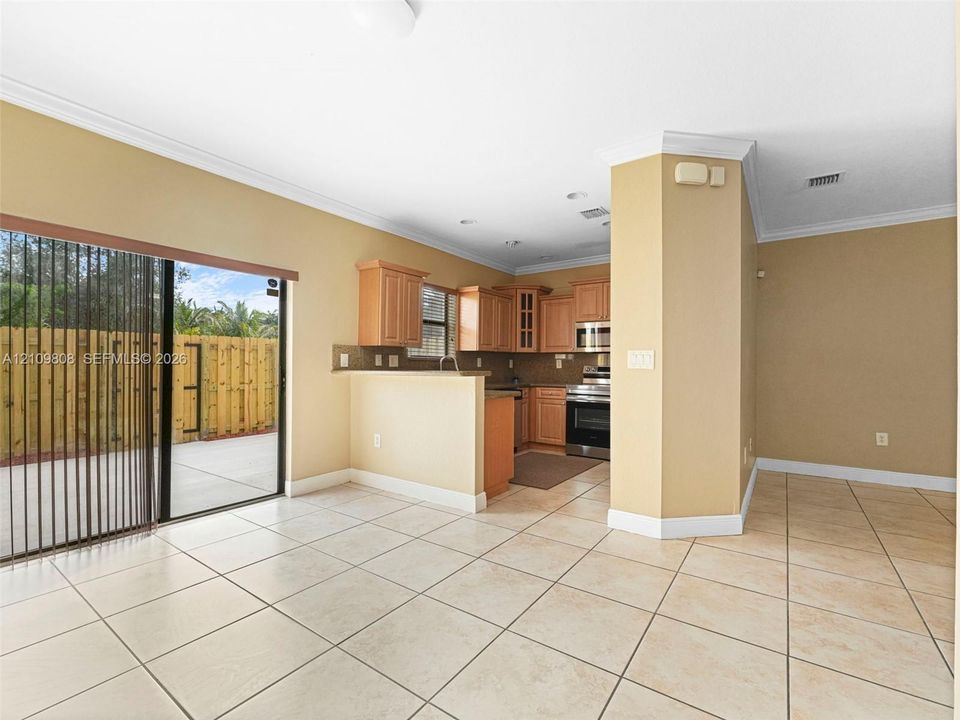 Kitchen featuring wood cabinetry, stainless steel appliances, tile flooring, crown molding, and sliding glass doors to a patio