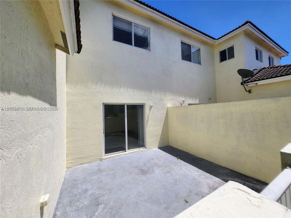 Stucco exterior courtyard featuring a paved patio, sliding glass door, and perimeter privacy wall