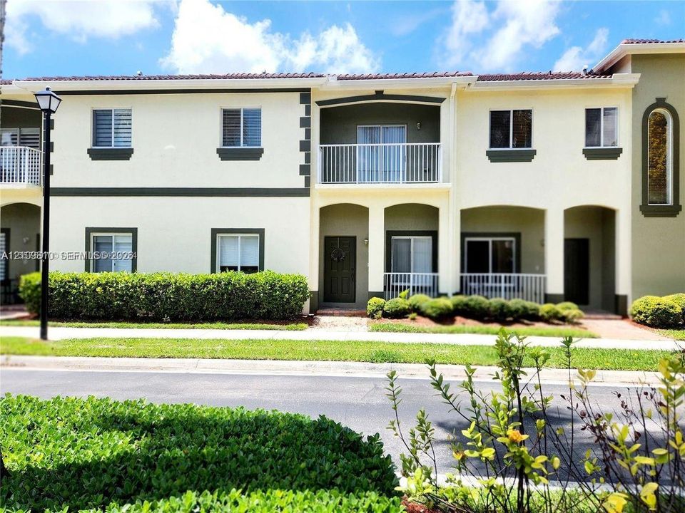 Two-story exterior featuring light-toned stucco walls with contrasting trim, a tiled roof, a private upper-level balcony with white railings, and covered lower-level entryways