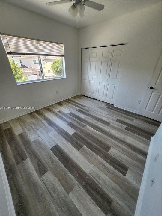 Room featuring wood-finish flooring, a bi-fold closet with panel doors, and a ceiling fan with integrated lighting