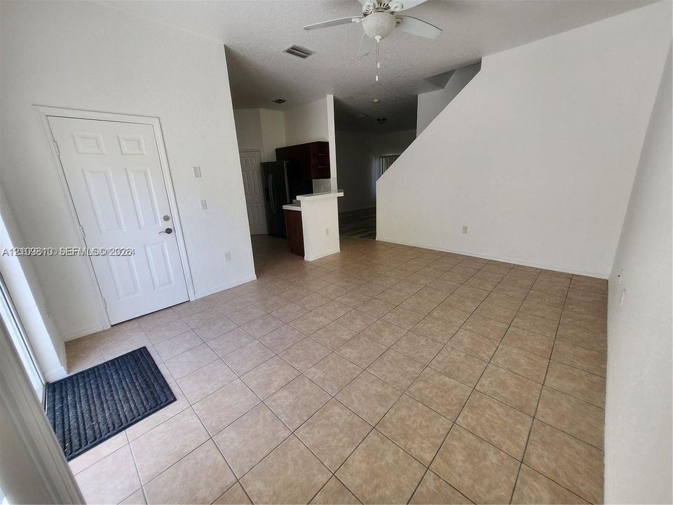 Open floor plan featuring tile flooring, a white-paneled entry door, a ceiling fan, and a kitchen island with dark cabinetry