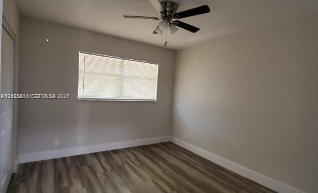 Neutral-toned interior space featuring wood-finish flooring, a ceiling fan with integrated lighting, and a single-panel interior door