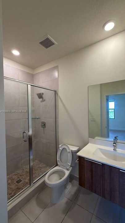 Floating vanity with wood-finish cabinetry and integrated sink, shower with glass enclosure and neutral-tone tile surround, and recessed ceiling lighting