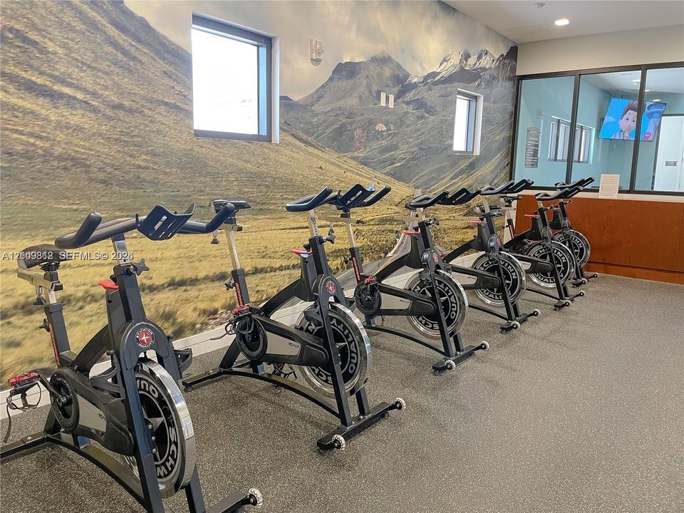 Fitness center featuring stationary exercise bicycles, durable flooring, mountain landscape wall mural, and glass partitions