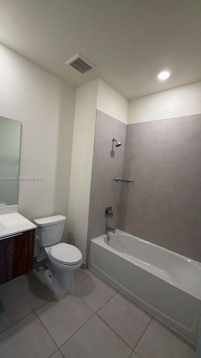 Bathroom featuring a wood-finish vanity with a white countertop, a white soaking tub, large-format tile shower surround, and ceramic tile flooring