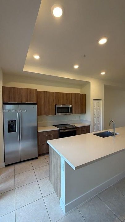 Kitchen featuring wood-finish cabinetry, stone-surface countertops, an integrated island with a stainless steel sink, stainless steel appliances, and recessed lighting
