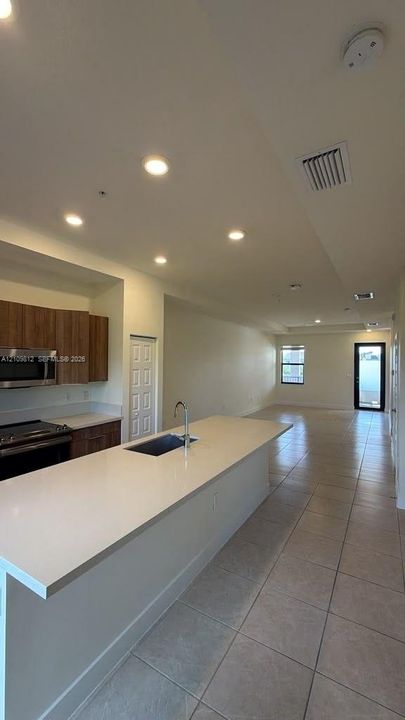 Kitchen featuring an island with a stone-finish countertop, undermount sink, recessed lighting, wood-finish cabinetry, and ceramic tile flooring