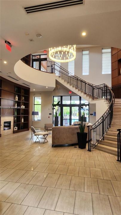 Grand foyer featuring a sweeping curved staircase with wrought-iron railing, floor-to-ceiling built-in shelving, tile flooring, and a tiered chandelier