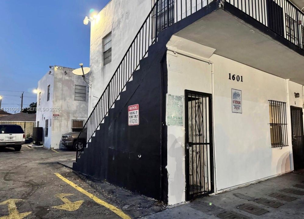 Multi-story stucco exterior with external metal staircase, black metal security door, and window security bars