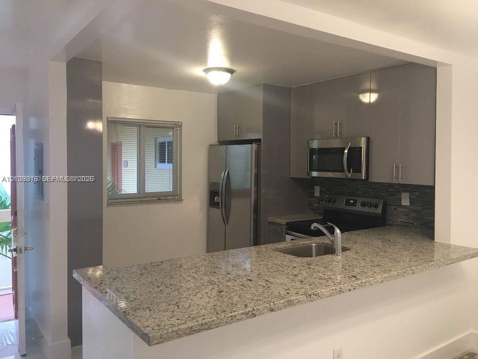 Kitchen featuring high-gloss cabinetry, stone-finish countertops, stainless steel appliances, a tile backsplash, and a breakfast bar