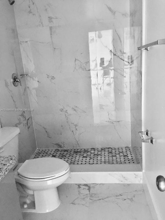 Walk-in shower featuring large-format stone-look wall tiles, a penny-round tile shower floor, chrome fixtures, a glass shower panel, and coordinating stone-look flooring