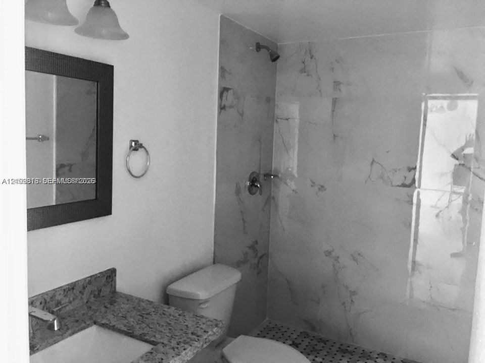 Bathroom featuring a stone-topped vanity, wall-mounted mirror, polished chrome fixtures, and a walk-in shower finished with large-format stone wall tiles