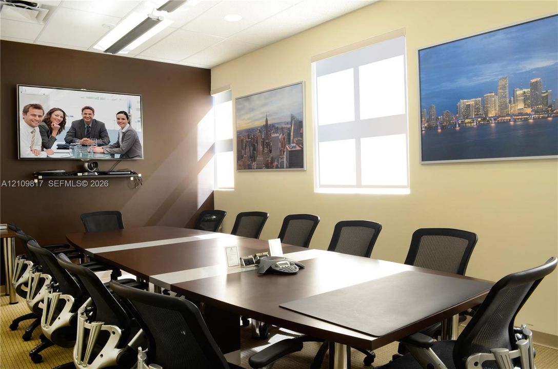 Conference room featuring a dark-toned accent wall, large-format wall-mounted display, recessed ceiling lighting, and multiple windows