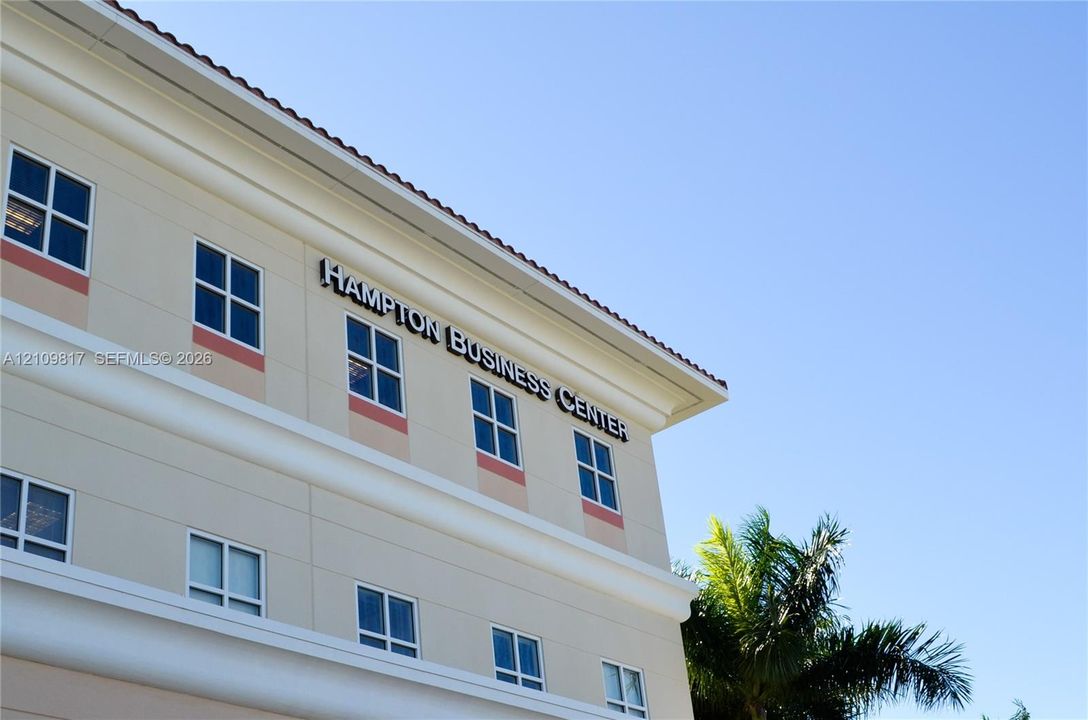 Multi-story exterior featuring a light-toned stucco facade, decorative horizontal banding, a tiled roofline, and grid-patterned windows