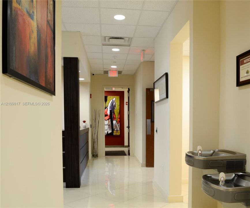 Hallway featuring recessed lighting, a suspended drop ceiling, polished tile flooring, and a wall-mounted dual-level water fountain