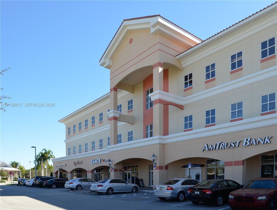 Three-story commercial exterior featuring a stucco facade, covered ground-floor arcade, architectural pediment, and multi-pane fenestration