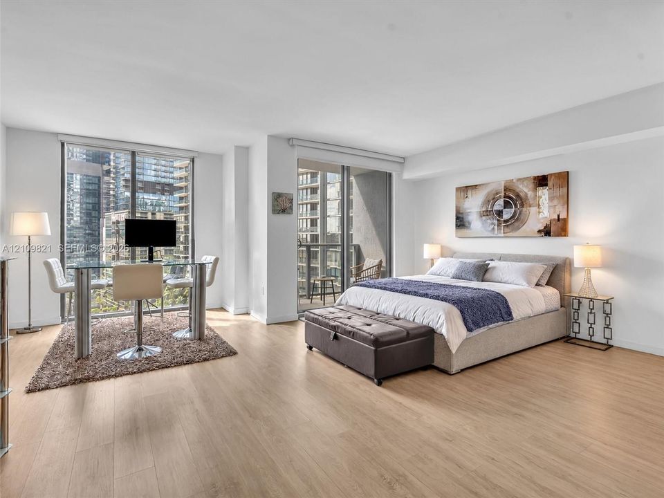 Floor-to-ceiling windows, wood-finish flooring, and direct balcony access through sliding glass doors