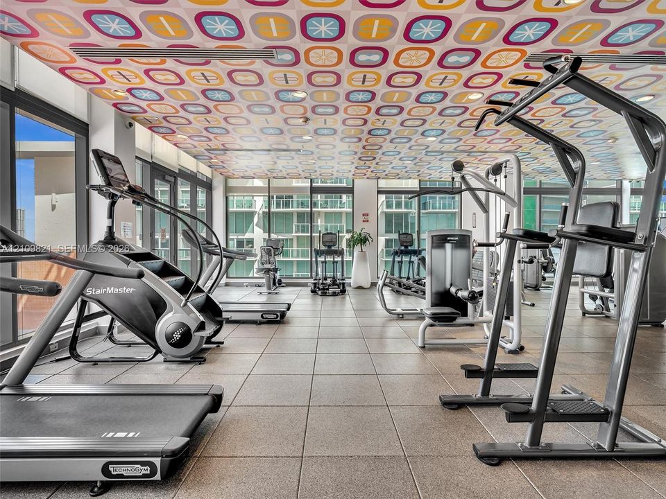 Fitness center featuring floor-to-ceiling windows, square tile flooring, and decorative patterned drop ceiling