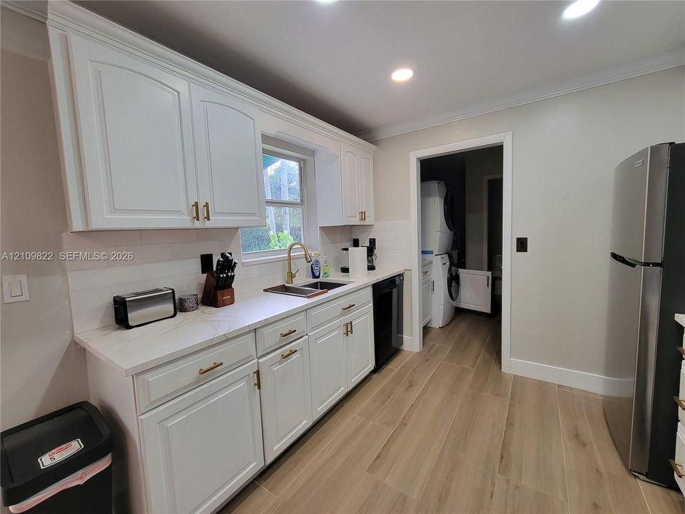 Kitchen featuring white shaker-style cabinetry, gold-tone hardware, light-toned countertops, subway tile backsplash, and wood-finish flooring