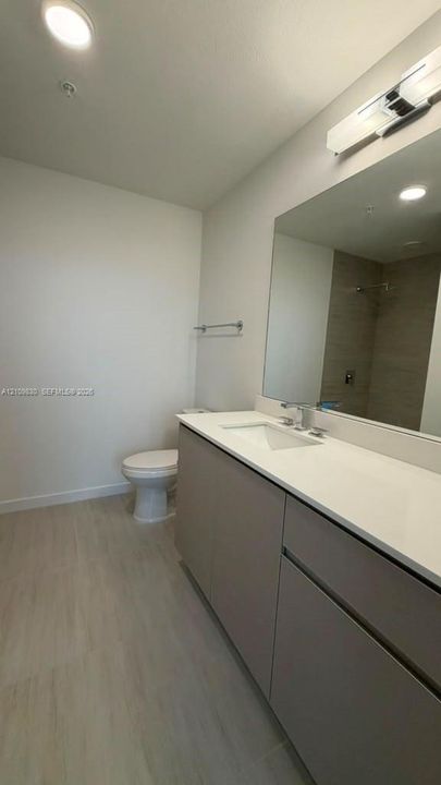 Bathroom featuring a vanity with a white countertop and rectangular undermount sink, flat-panel cabinetry, large wall-mounted mirror, overhead light fixture, and tile flooring