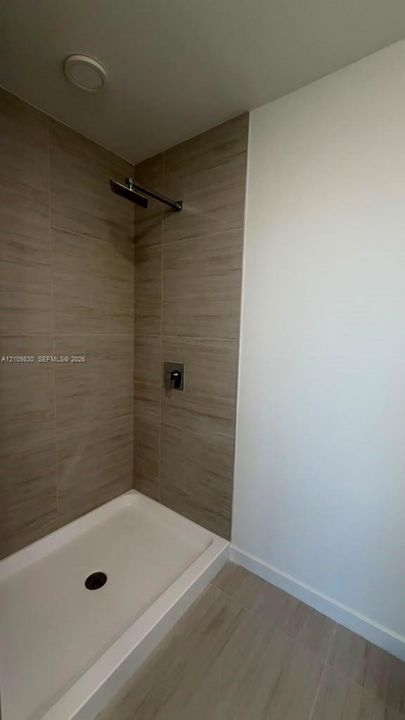 Shower featuring floor-to-ceiling wood-finish tile surround, white low-profile basin, and modern wall-mounted rainfall showerhead