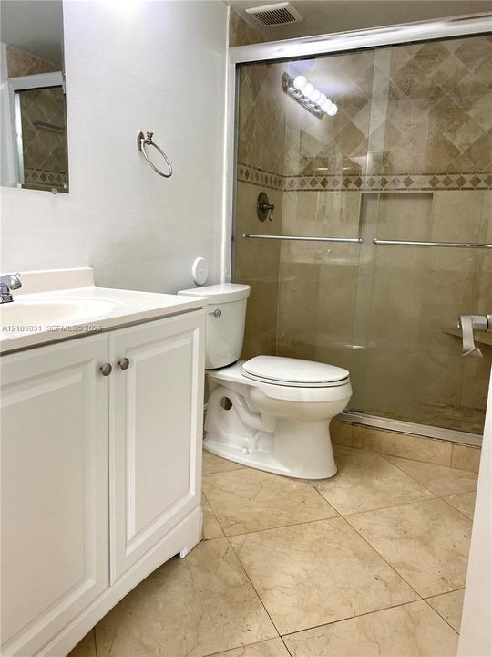 Bathroom featuring a white vanity cabinet, solid-surface countertop, tiled shower enclosure with sliding glass doors, and diagonal-pattern floor tiling
