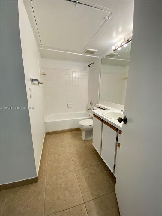 Bathroom featuring tile flooring, a shower-tub combination with wall tile surround, a built-in vanity with a circular basin, and a large-format mirror