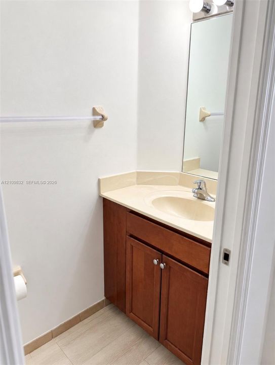 Wood-finish cabinetry, solid-surface countertop with integrated oval basin, polished chrome faucet, rectangular wall-mounted mirror, and multi-light fixture