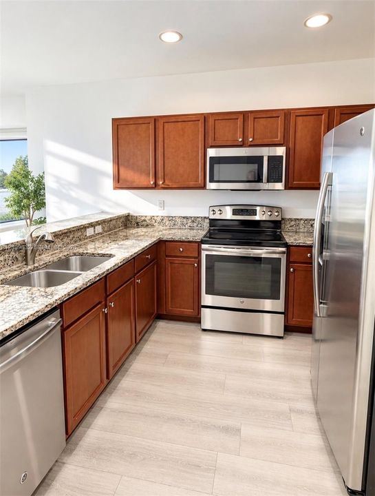 Kitchen featuring wood cabinetry, stone-finish countertops, stainless steel appliances, a double-basin undermount sink, and wood-finish flooring