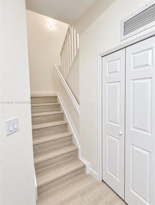 Staircase featuring wood-finish treads and a white wooden balustrade, paired with a white paneled bifold closet door