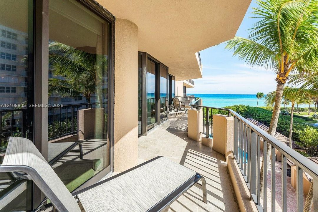 Covered balcony featuring tile flooring, full-height glass sliding doors, and metal railings, overlooking the ocean