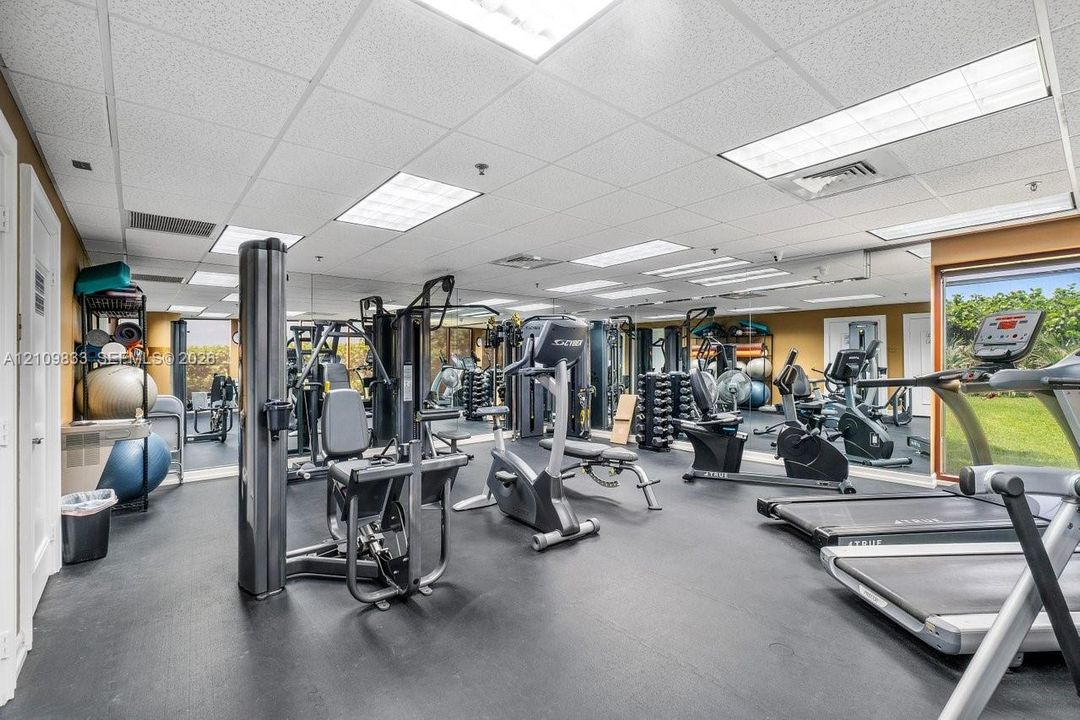Fitness center featuring rubber flooring, mirrored walls, drop ceiling panels, and floor-to-ceiling windows