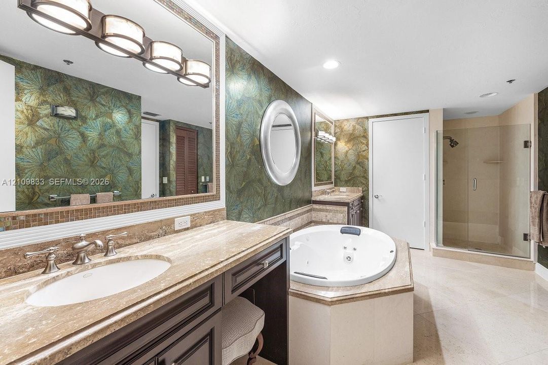 Bathroom featuring a stone-topped vanity with undermount sink, jetted soaking tub, glass-enclosed shower, decorative wall coverings, and integrated lighting fixtures
