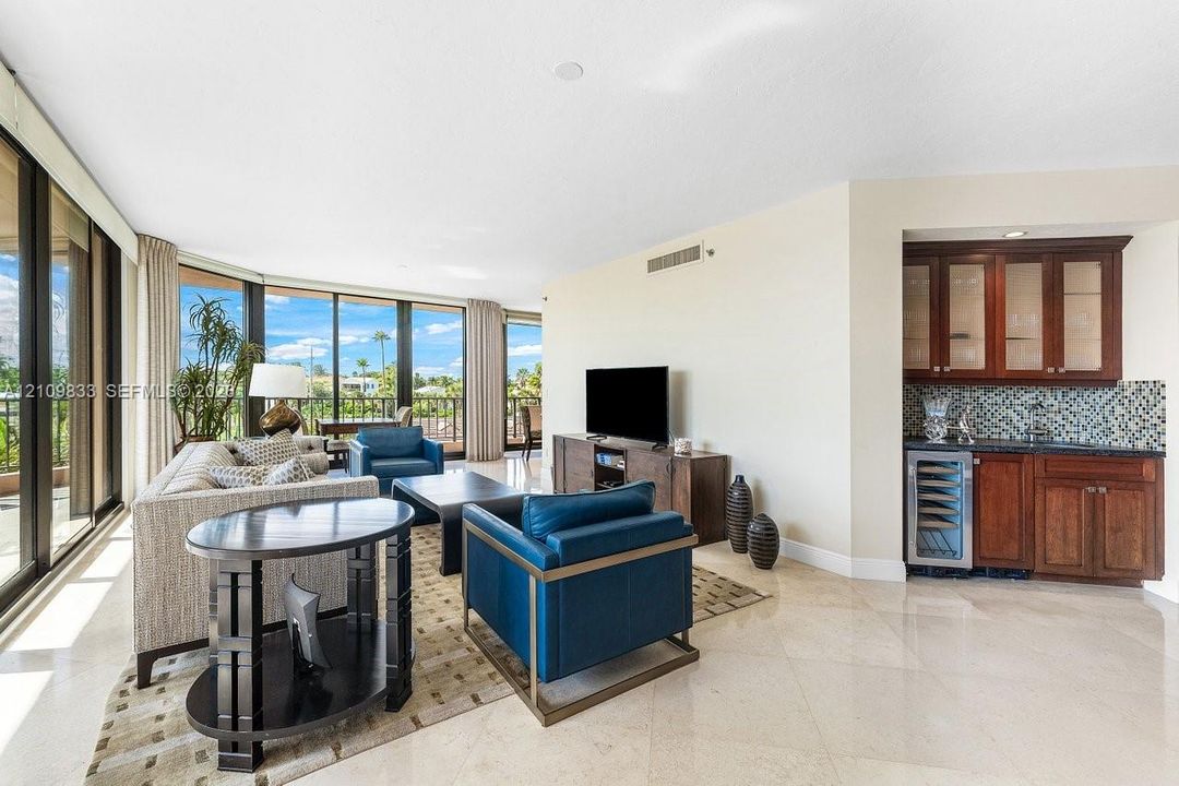 Floor-to-ceiling windows, polished stone flooring, and a built-in wet bar featuring dark wood cabinetry, glass-front upper cabinets, a mosaic tile backsplash, and an integrated under-counter beverage refrigerator