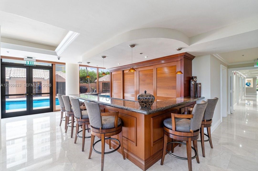 Custom wood cabinetry bar featuring a stone countertop, recessed ceiling lighting, pendant fixtures, and polished tile flooring