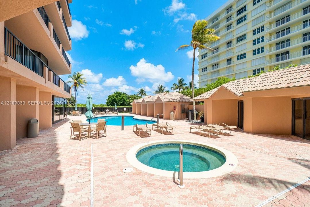 Community pool area featuring an in-ground spa, paver deck, and covered poolside cabanas