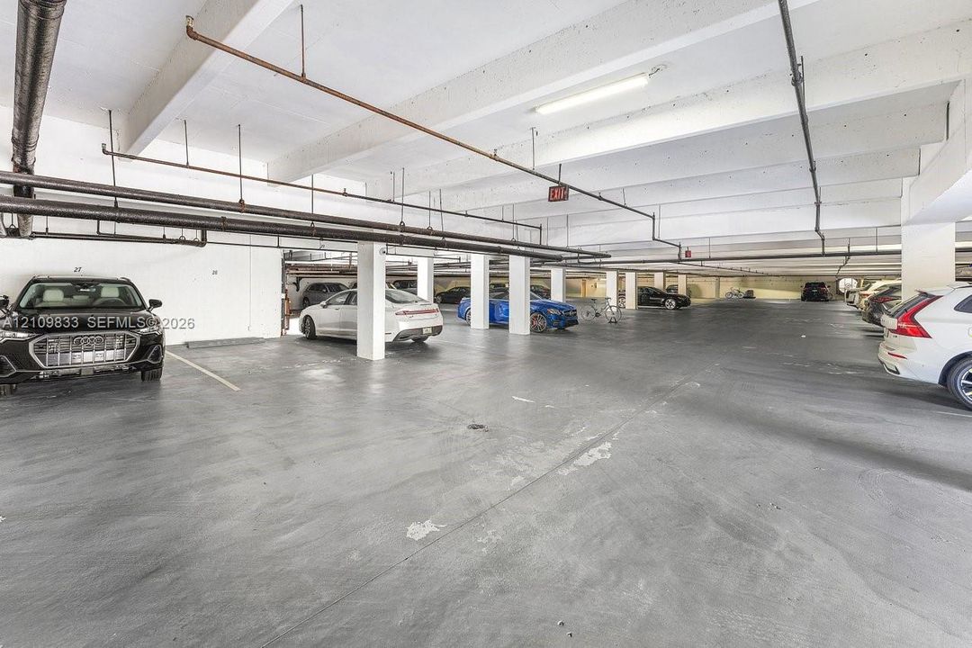 Covered parking garage featuring concrete flooring, structural support columns, and overhead linear lighting fixtures