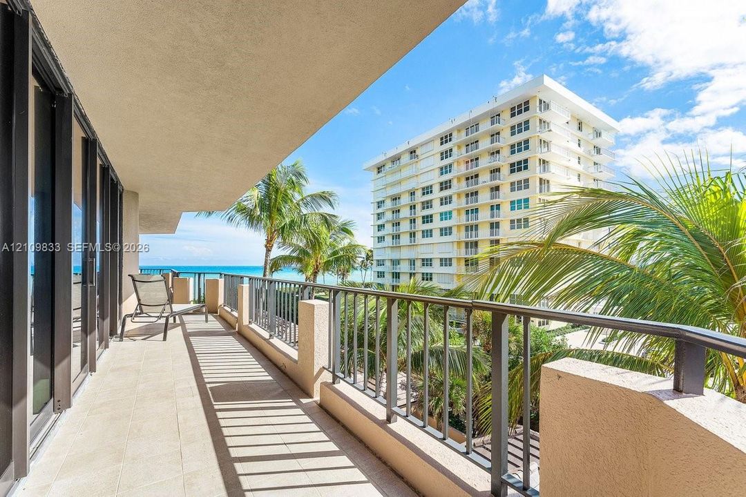 Covered balcony featuring tile flooring and metal railings, overlooking palm trees and the ocean