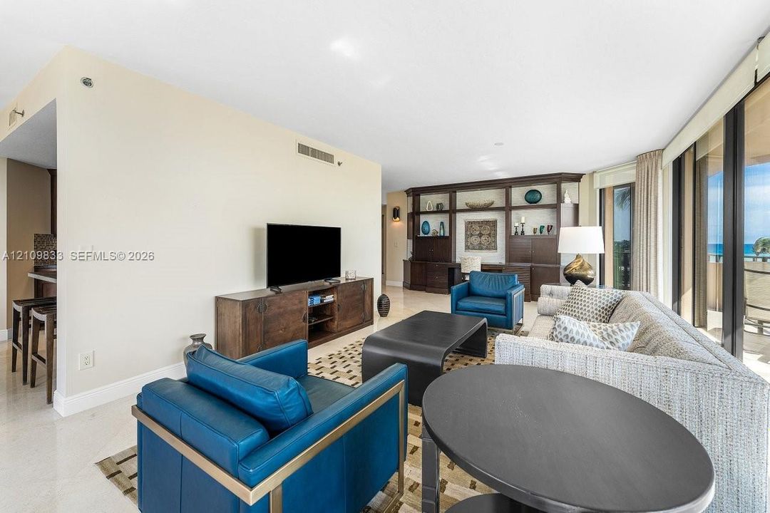 Open-concept interior featuring large-format stone flooring, floor-to-ceiling glass panel windows, and custom built-in dark wood shelving with integrated storage
