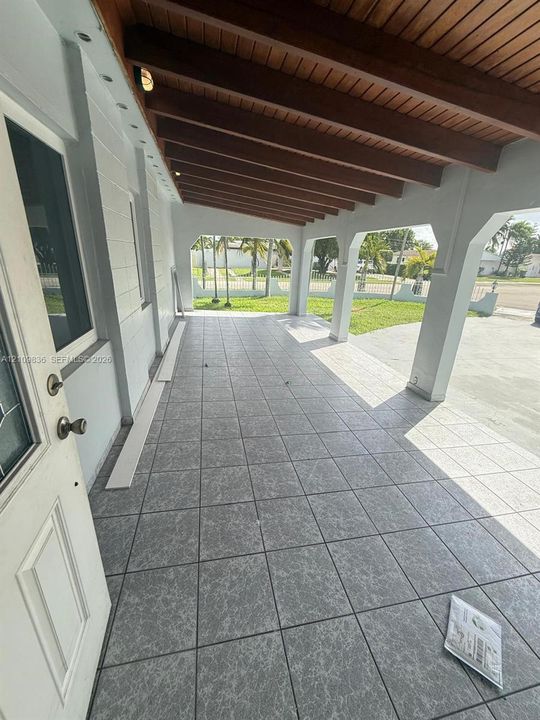 Covered porch featuring a wood-beam ceiling, tiled flooring, arched structural supports, and concrete masonry exterior walls