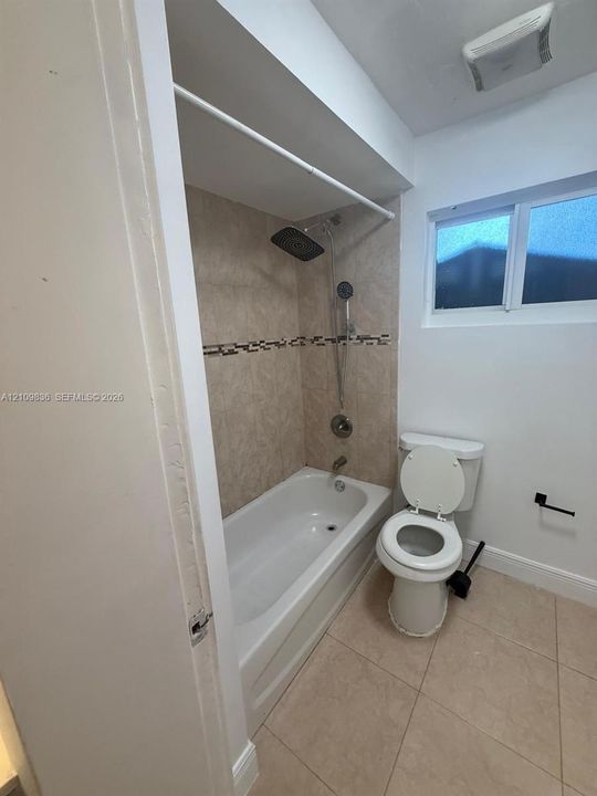 Full bathroom featuring a white porcelain tub, shower system with a rectangular rainfall showerhead and handheld attachment, stone-tiled tub surround with decorative mosaic accent, and neutral floor tiling