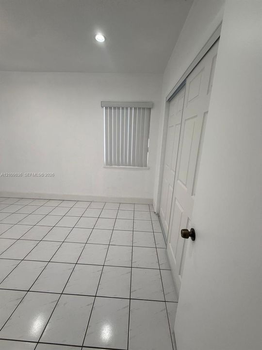 Room featuring neutral tile flooring, recessed ceiling lighting, and a closet with white paneled sliding doors