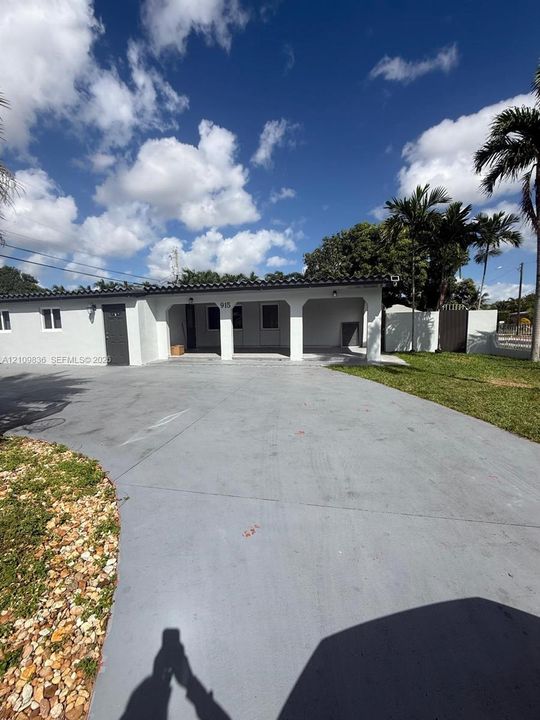 Single-story exterior featuring a white stucco facade, a dark-toned tile roof, an integrated covered entryway, a wide concrete driveway, and white decorative columns