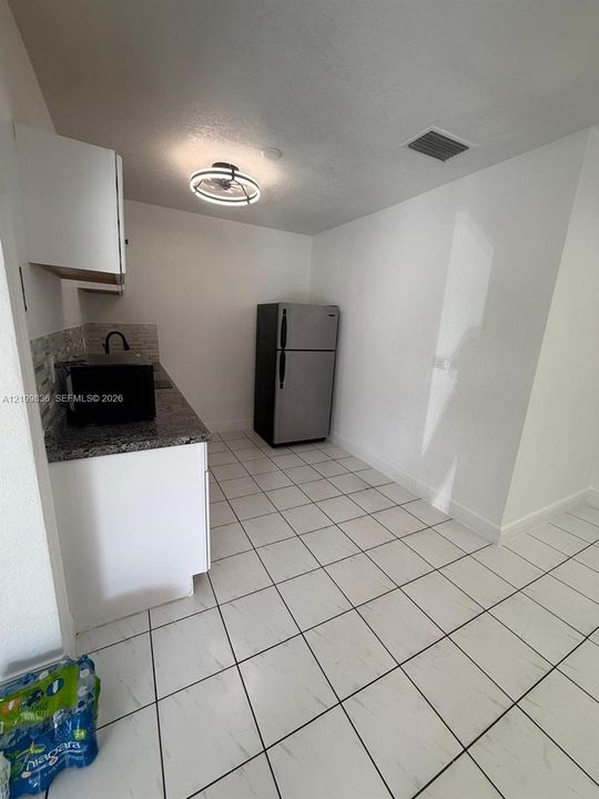 Kitchen featuring white cabinetry, stone-finish countertops, tile backsplash, stainless steel refrigerator, and tiled flooring