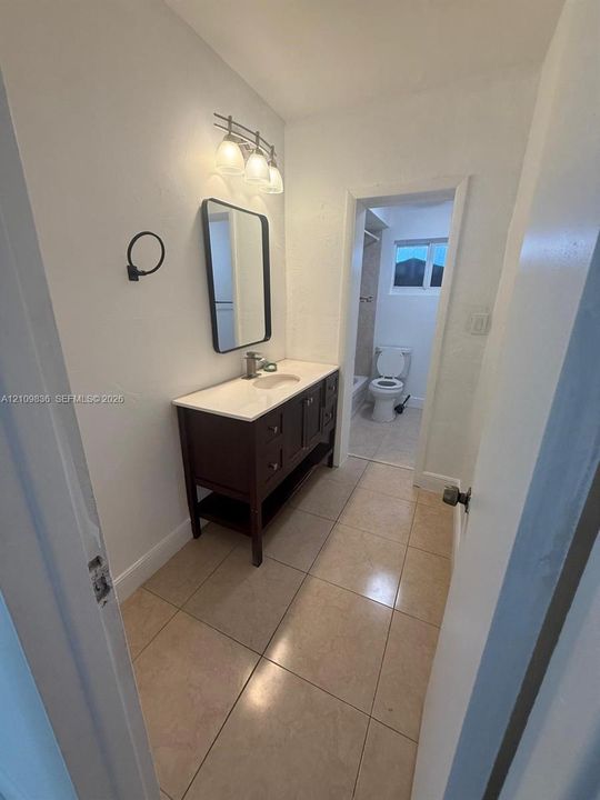 Dark wood vanity featuring a light-toned countertop, rectangular wall-mounted mirror, three-light fixture, and ceramic tile flooring
