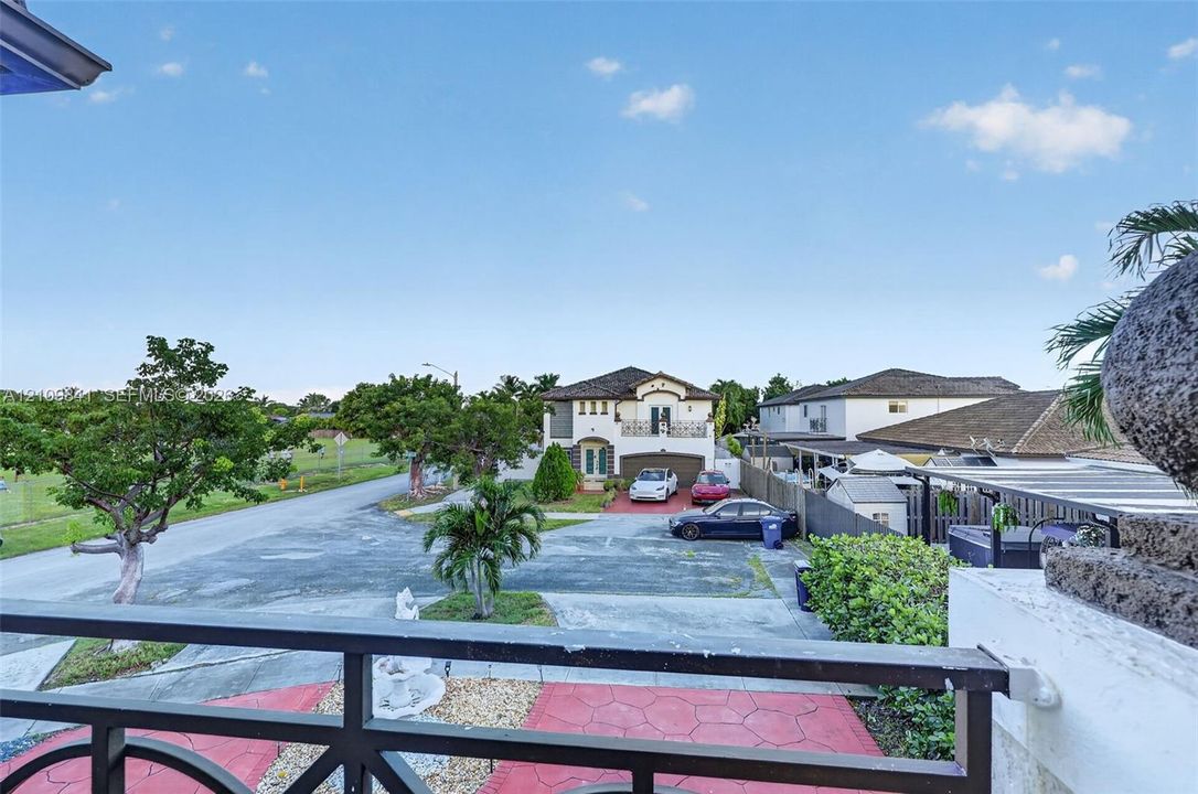 Two-story residence featuring a paved driveway, decorative stamped concrete surfaces, a metal balcony railing, and mature palm landscaping