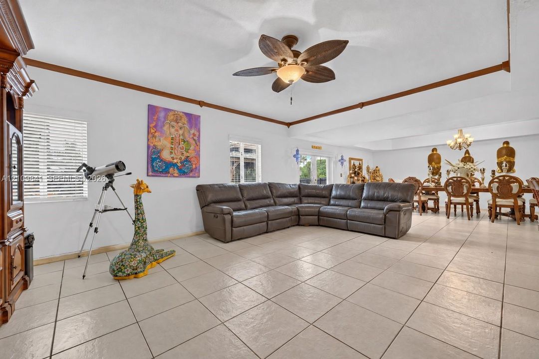 Open-concept interior featuring large-format tile flooring, tray ceilings with crown molding, a ceiling fan with leaf-style blades, and integrated chandeliers
