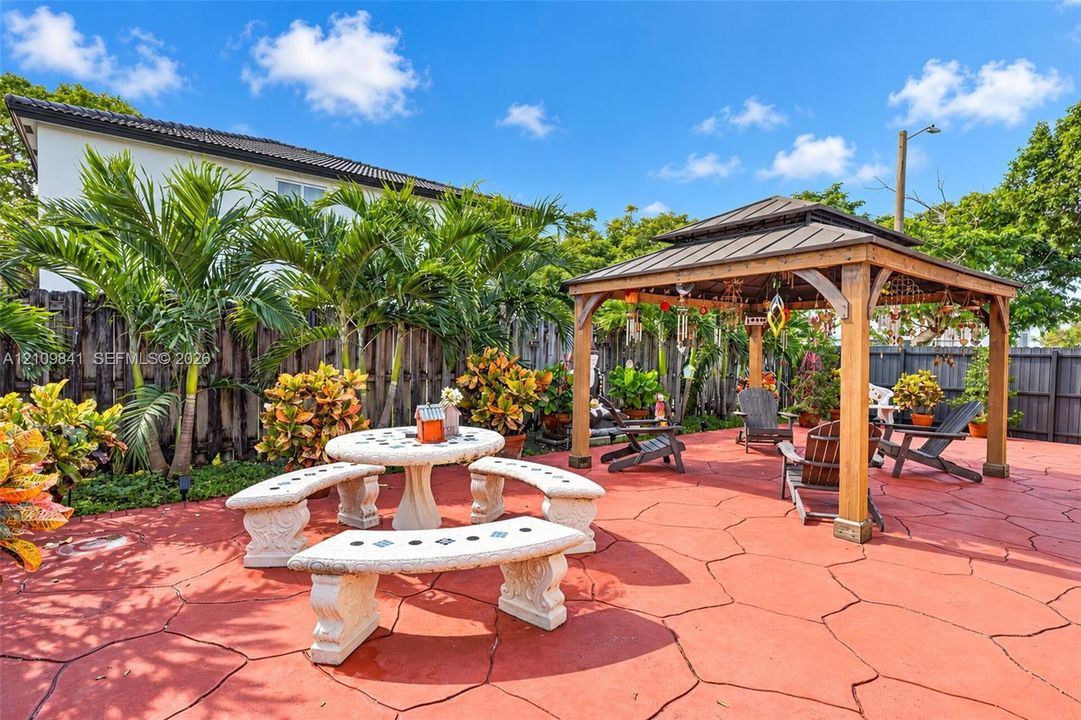 Expansive patio featuring stamped concrete, a wooden gazebo with a metal roof, and a perimeter privacy fence