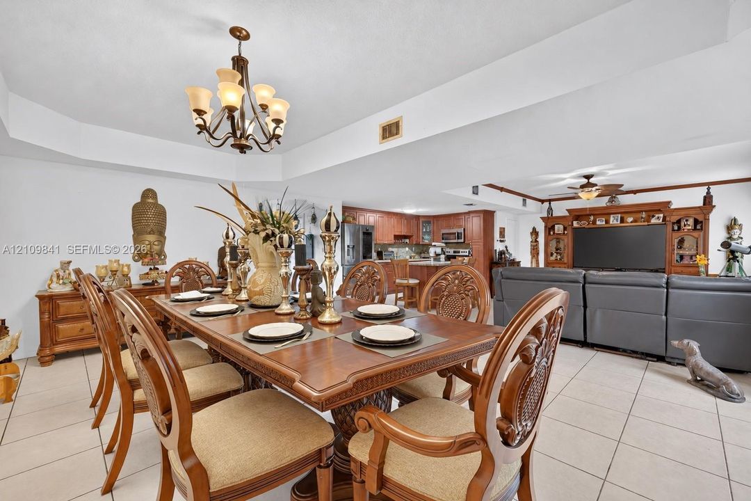Open-concept interior featuring tray ceilings, neutral tile flooring, a multi-arm chandelier, and built-in wood cabinetry